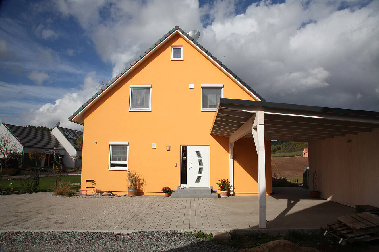 Aischtaler Holzhaus Sonnenenergiehaus mit sonnengelber Fassade, Eingangsbereich mit Carport und moderner Haustür