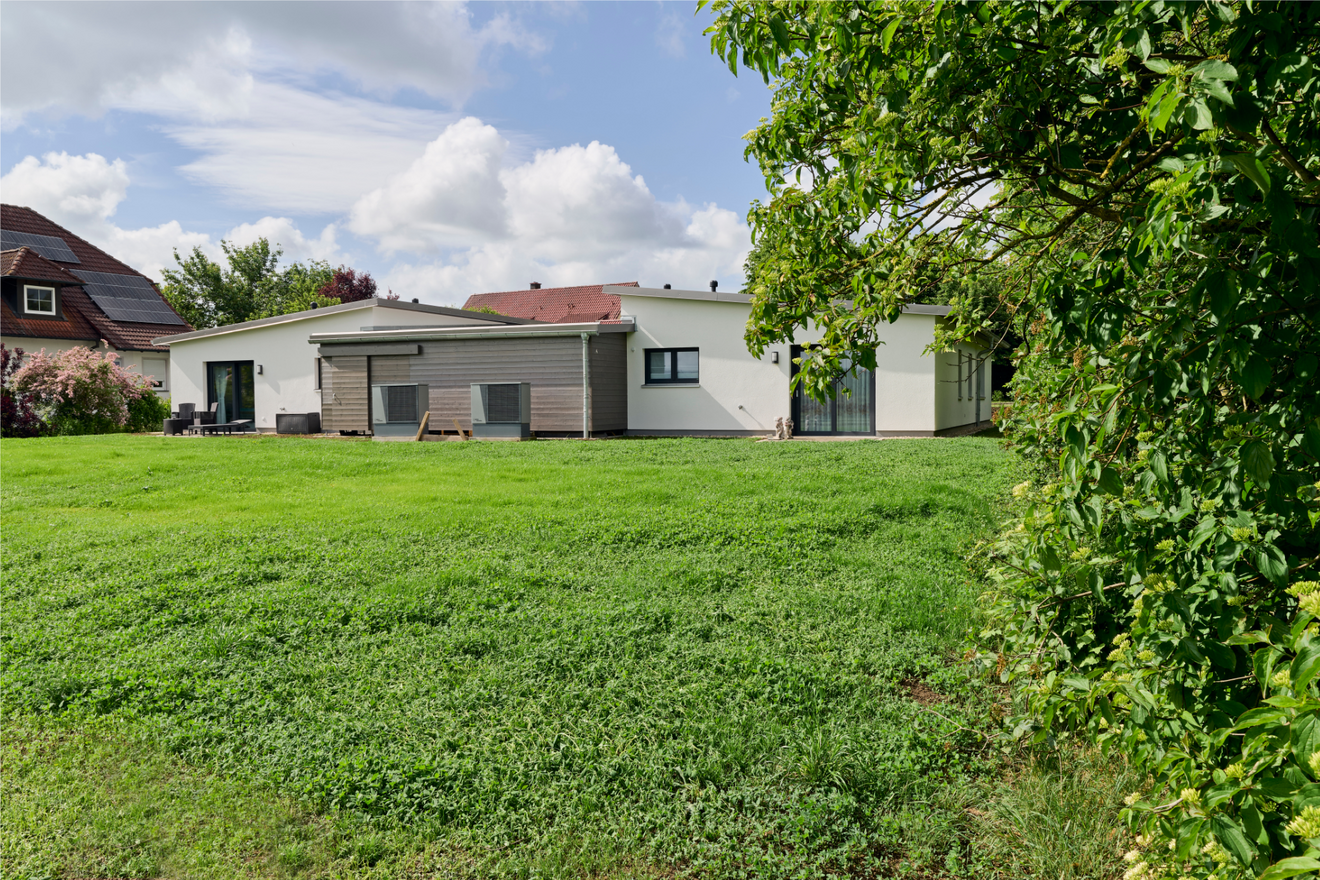 Rückansicht des Tandemhauses von Aischtaler Holzhaus mit ebenerdigem Zugang, Holzfassade und angrenzendem Rasenbereich.
