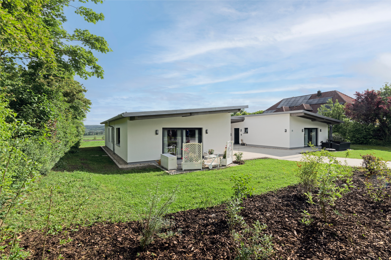 Rückseite des Tandemhauses von Aischtaler Holzhaus mit zwei separaten Terrassen, Sitzmöbeln und Blick ins Grüne.