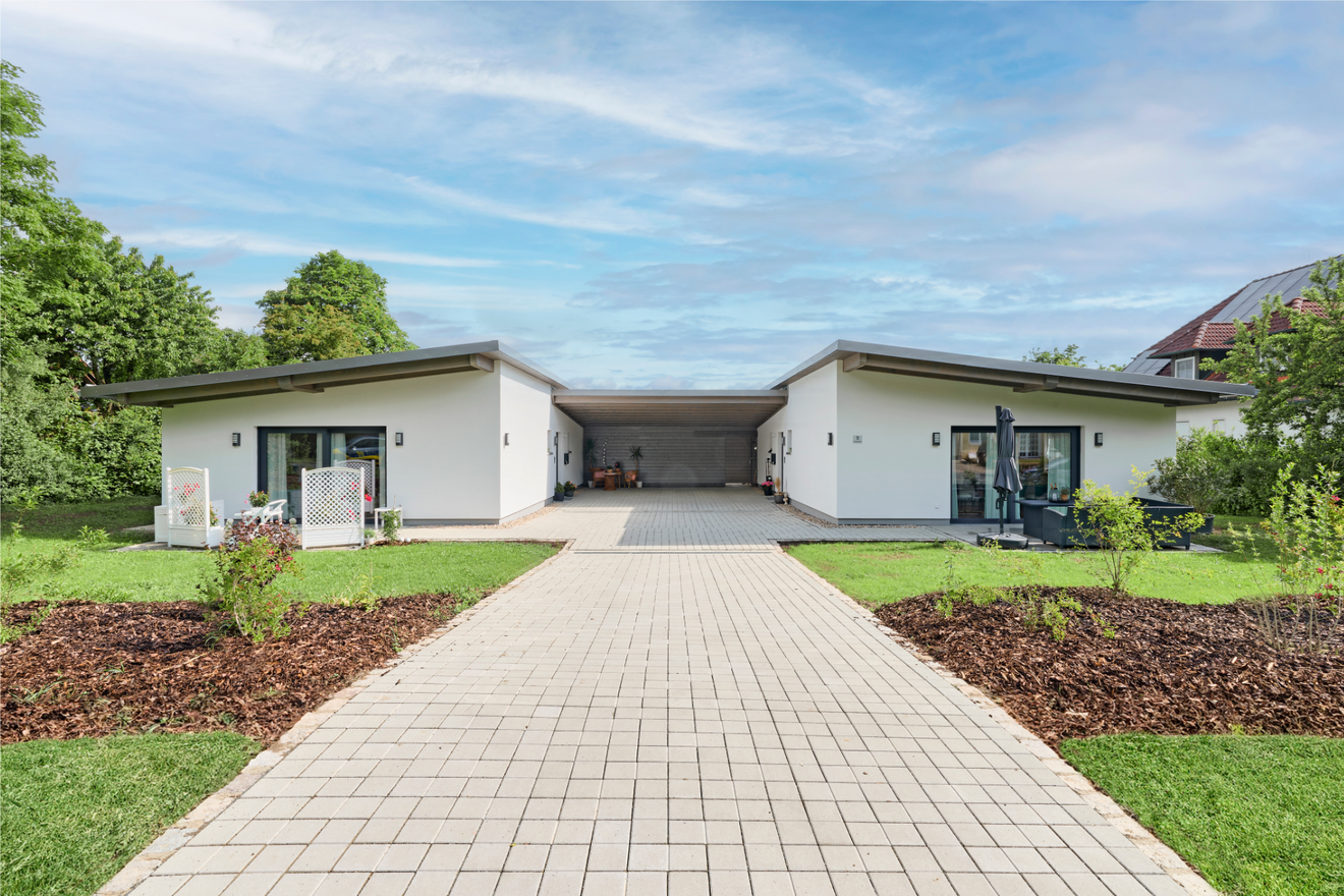 Frontansicht des Tandemhauses von Aischtaler Holzhaus mit zwei getrennten Eingängen, überdachtem Carport und bepflanztem Vorgarten.