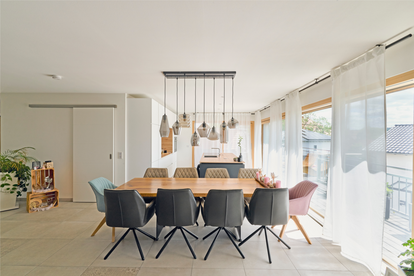 Langer Esstisch im Kubikhaus von Aischtaler Holzhaus mit Designleuchten und durchgehender Fensterfront.