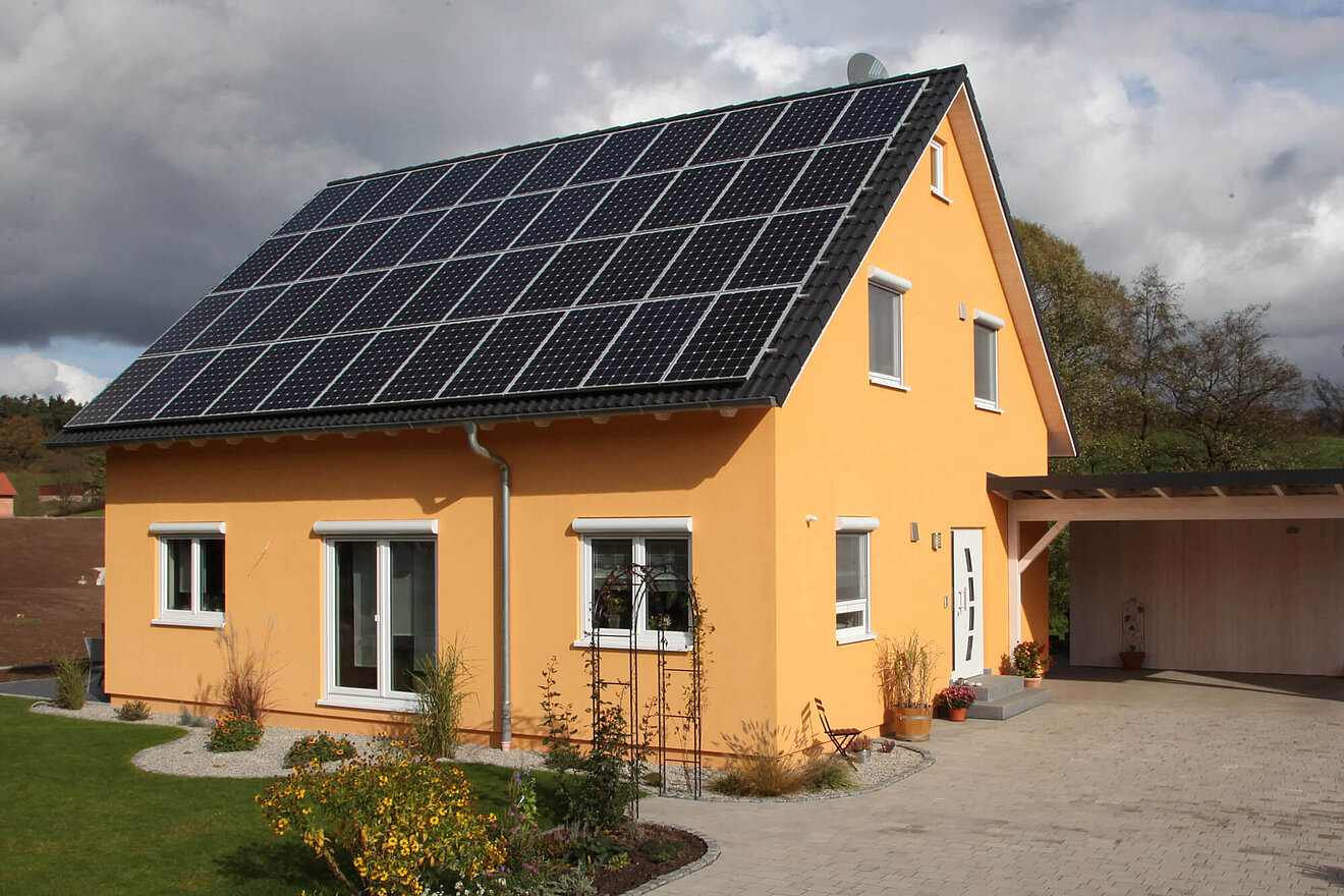 Aischtaler Holzhaus Sonnenenergiehaus mit Photovoltaikanlage auf dem Dach und sonnengelber Fassade, angrenzend an Carport und Garten