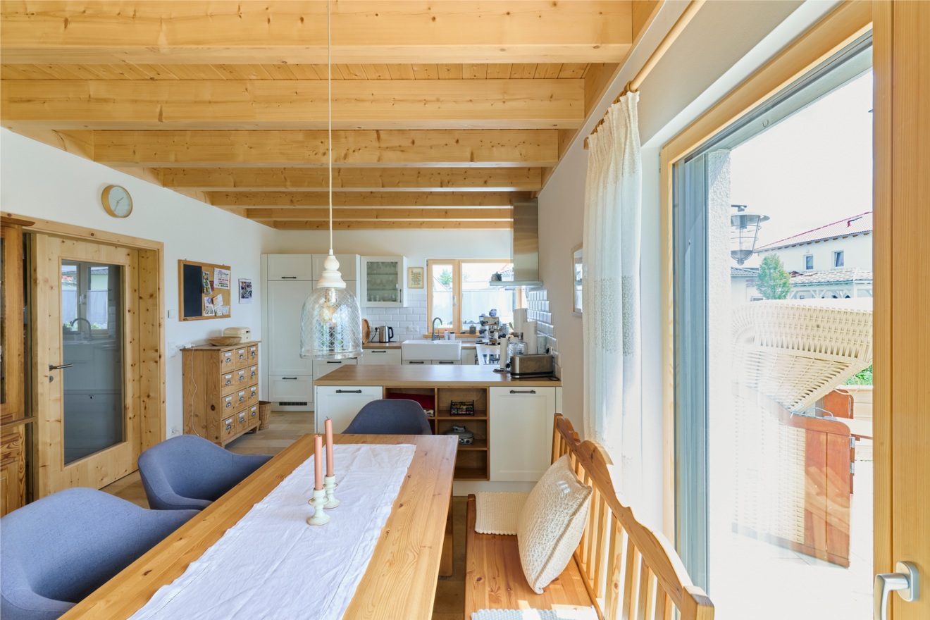 Esszimmer im Naturnah-Haus von Aischtaler Holzhaus mit Holztisch, blauen Sesseln und Blick zur Küche.