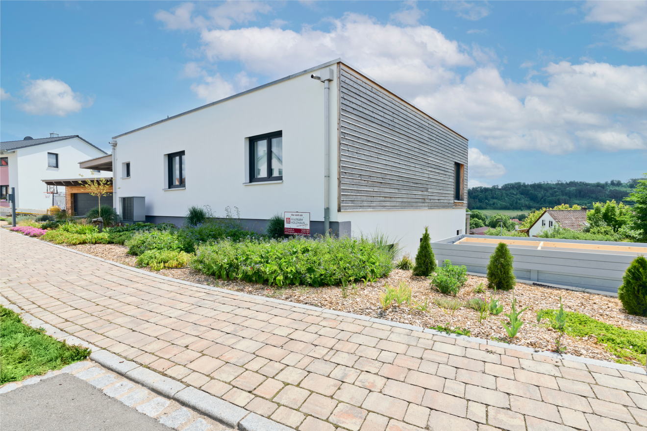 Kubikhaus von Aischtaler Holzhaus mit bepflanztem Vorgarten, Natursteinweg und vertäfelter Fassade.