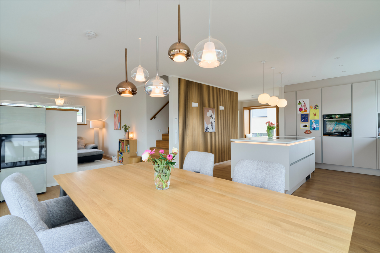 Moderne Küche im Freiraum-Haus von Aischtaler Holzhaus mit Kochinsel, Esstisch, Designerleuchten und Holzboden.