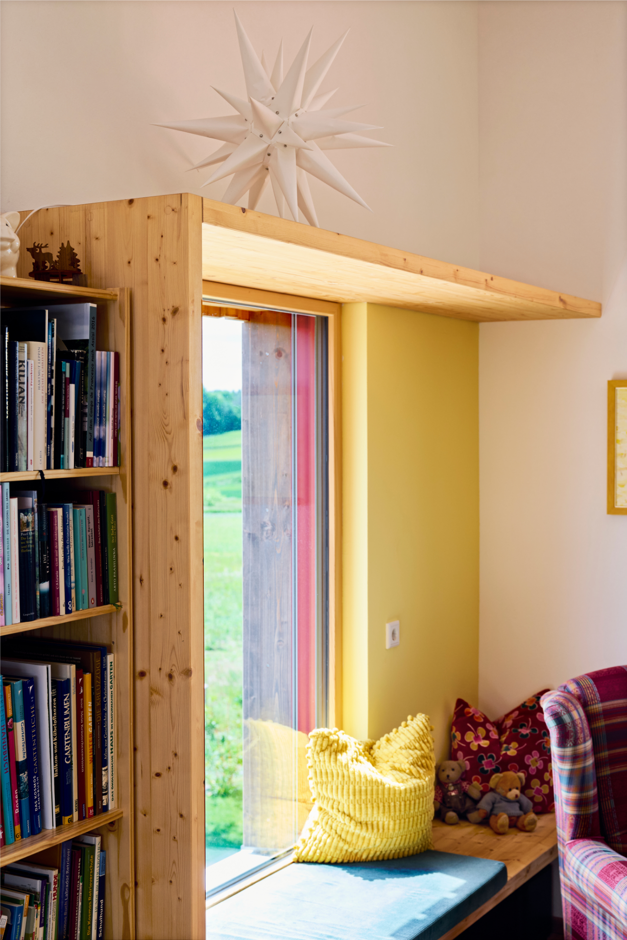 Gemütliche Leseecke im Naturnah-Haus von Aischtaler Holzhaus mit Fensterbank, gelbem Kissen und Bücherregal.