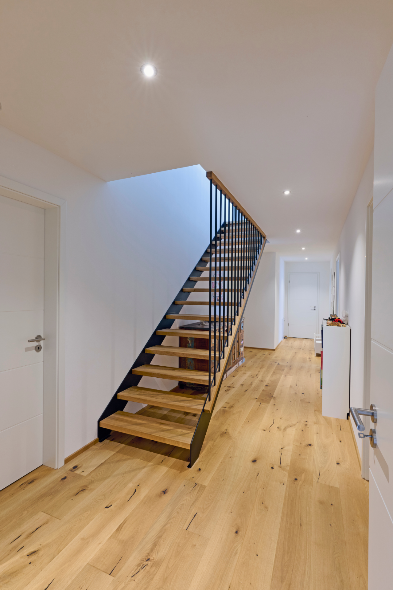 Moderne Holztreppe im Kubikhaus von Aischtaler Holzhaus mit schwarzem Metallgeländer und hellem Eichenboden.