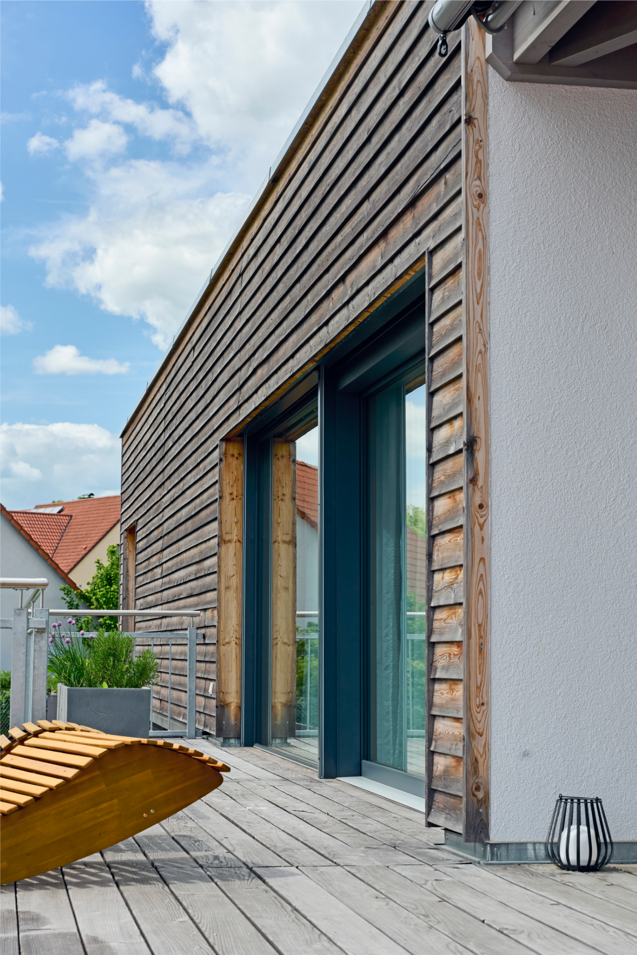 Terrasse am Kubikhaus von Aischtaler Holzhaus mit Holzdielen, Pflanzgefäßen und Holzfassade.