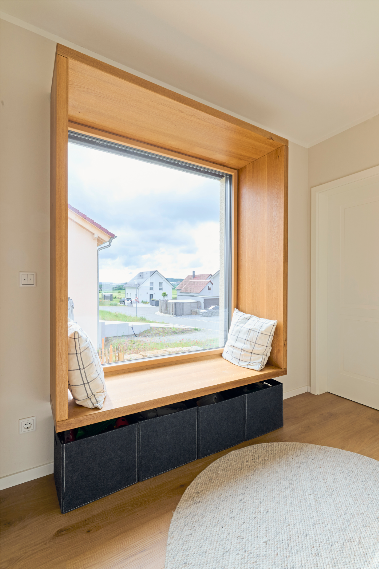 Große Fensterbank mit Holzrahmung im Freiraum-Haus von Aischtaler Holzhaus, ausgestattet mit Sitzkissen und darunter liegenden Stoffboxen.